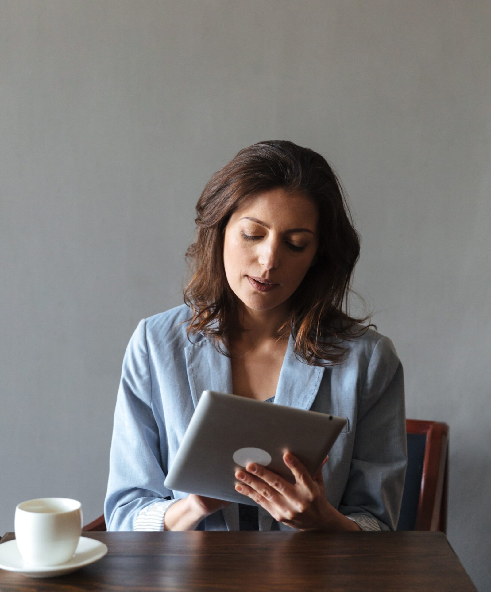 Picture of amazing woman sitting indoors. Looking aside using tablet computer.